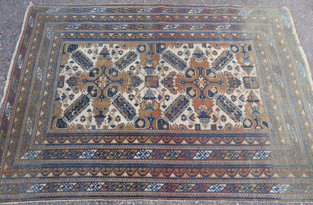 An antique hand-knotted Caucasian Kuba Seichur wool rug featuring a geometric white ground field surrounded by multi-layered patterned borders in blue, terracotta, and ochre. View IX