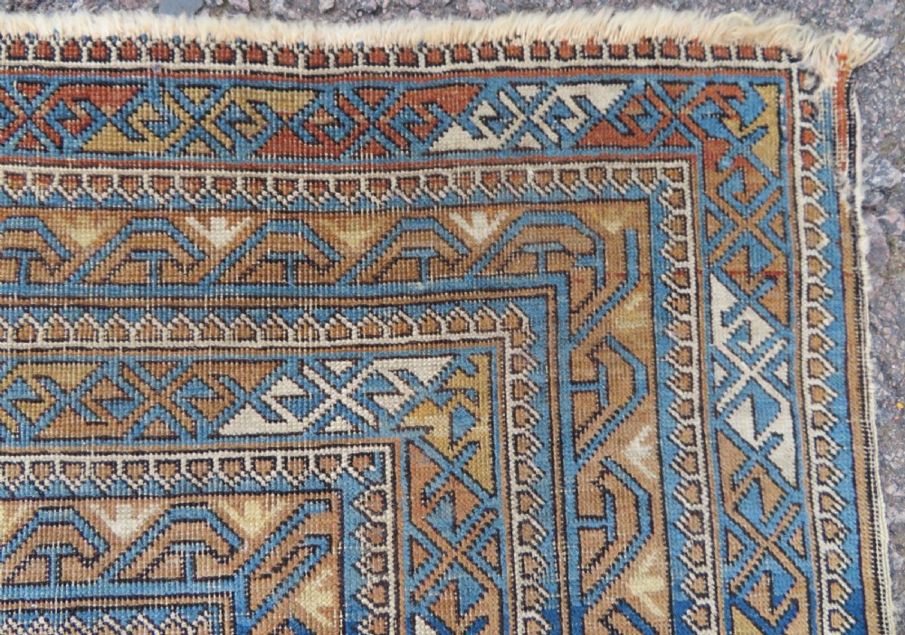 An antique hand-knotted Caucasian Kuba Seichur wool rug featuring a geometric white ground field surrounded by multi-layered patterned borders in blue, terracotta, and ochre. View X