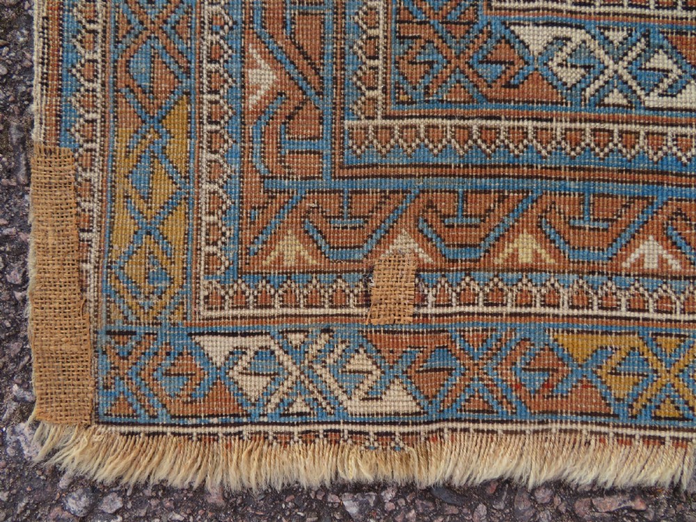 An antique hand-knotted Caucasian Kuba Seichur wool rug featuring a geometric white ground field surrounded by multi-layered patterned borders in blue, terracotta, and ochre. View XV