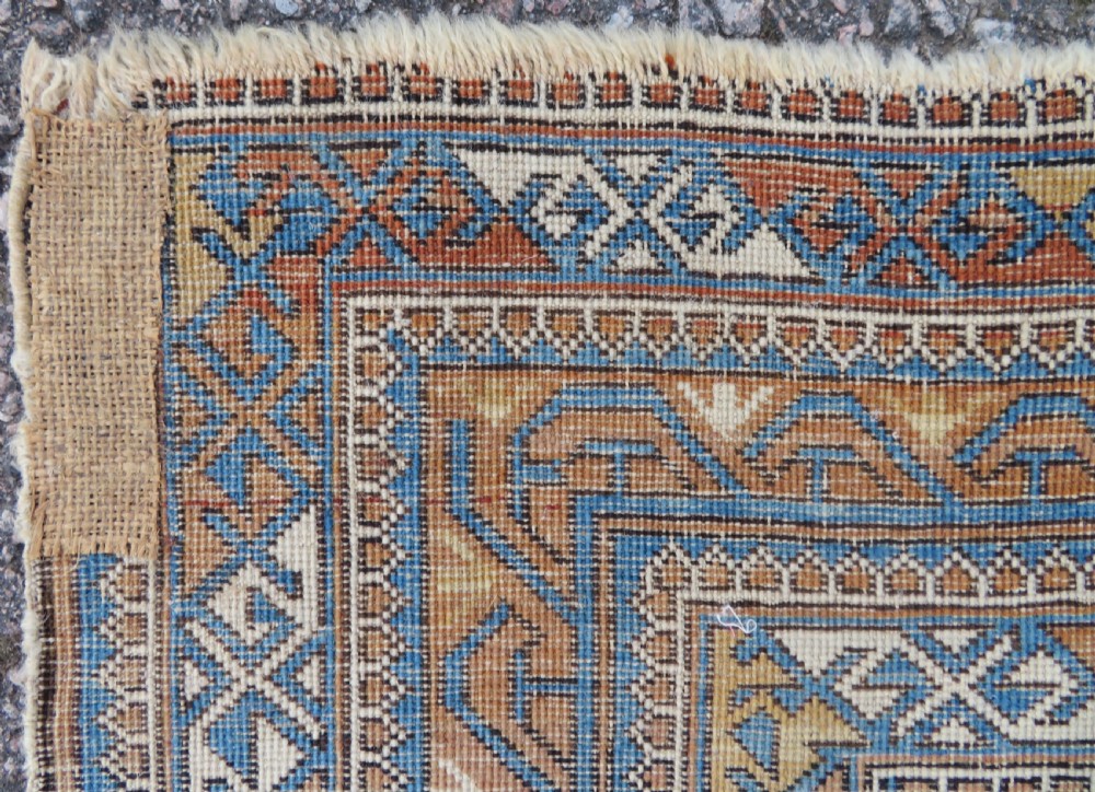An antique hand-knotted Caucasian Kuba Seichur wool rug featuring a geometric white ground field surrounded by multi-layered patterned borders in blue, terracotta, and ochre. View XVII
