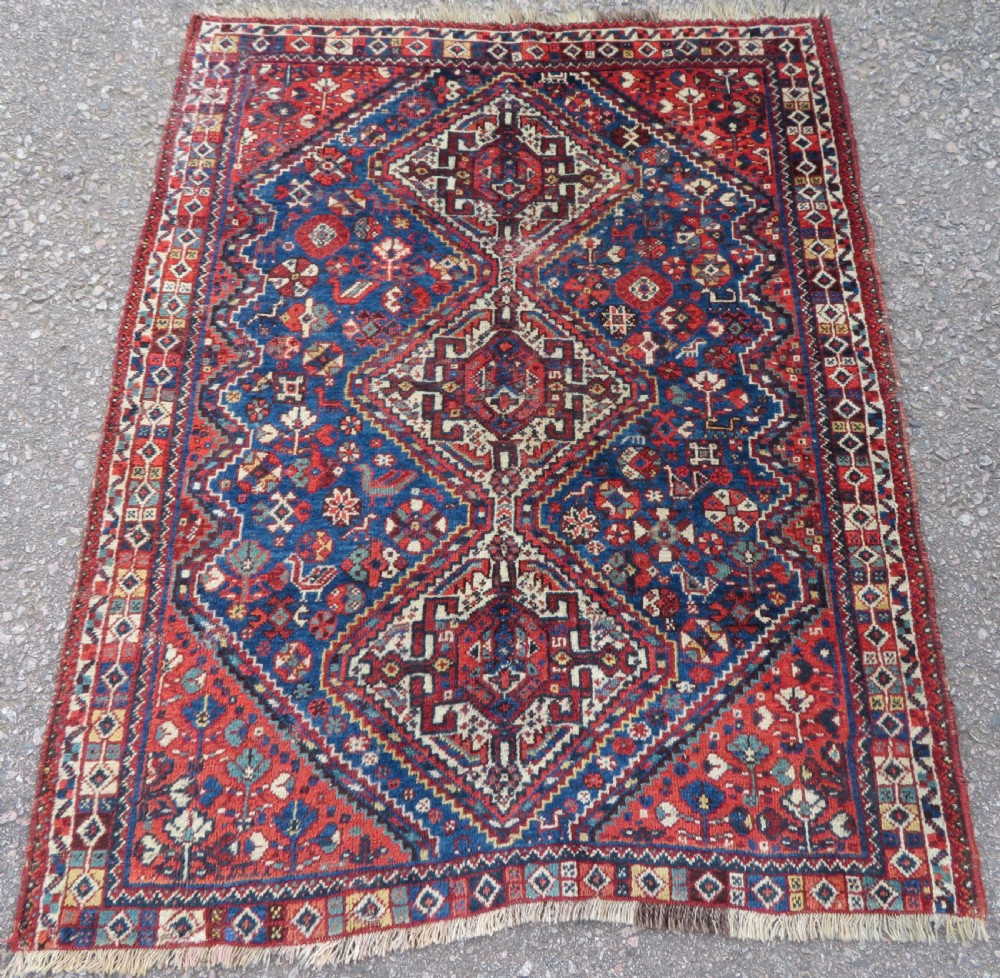 An antique South Persian Khamseh rug featuring three diamond-shaped central medallions and geometric bird motifs in shades of red, navy blue, and cream.