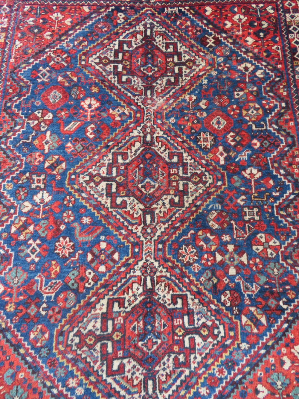 An antique South Persian Khamseh rug featuring three diamond-shaped central medallions and geometric bird motifs in shades of red, navy blue, and cream. View II