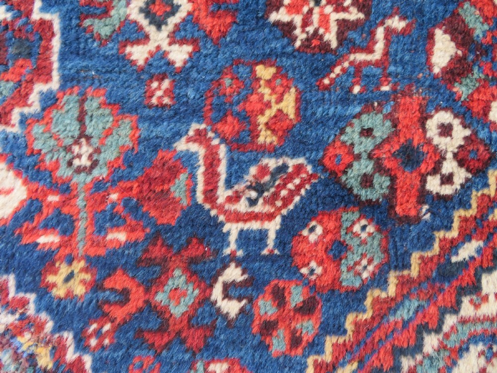 An antique South Persian Khamseh rug featuring three diamond-shaped central medallions and geometric bird motifs in shades of red, navy blue, and cream. View III