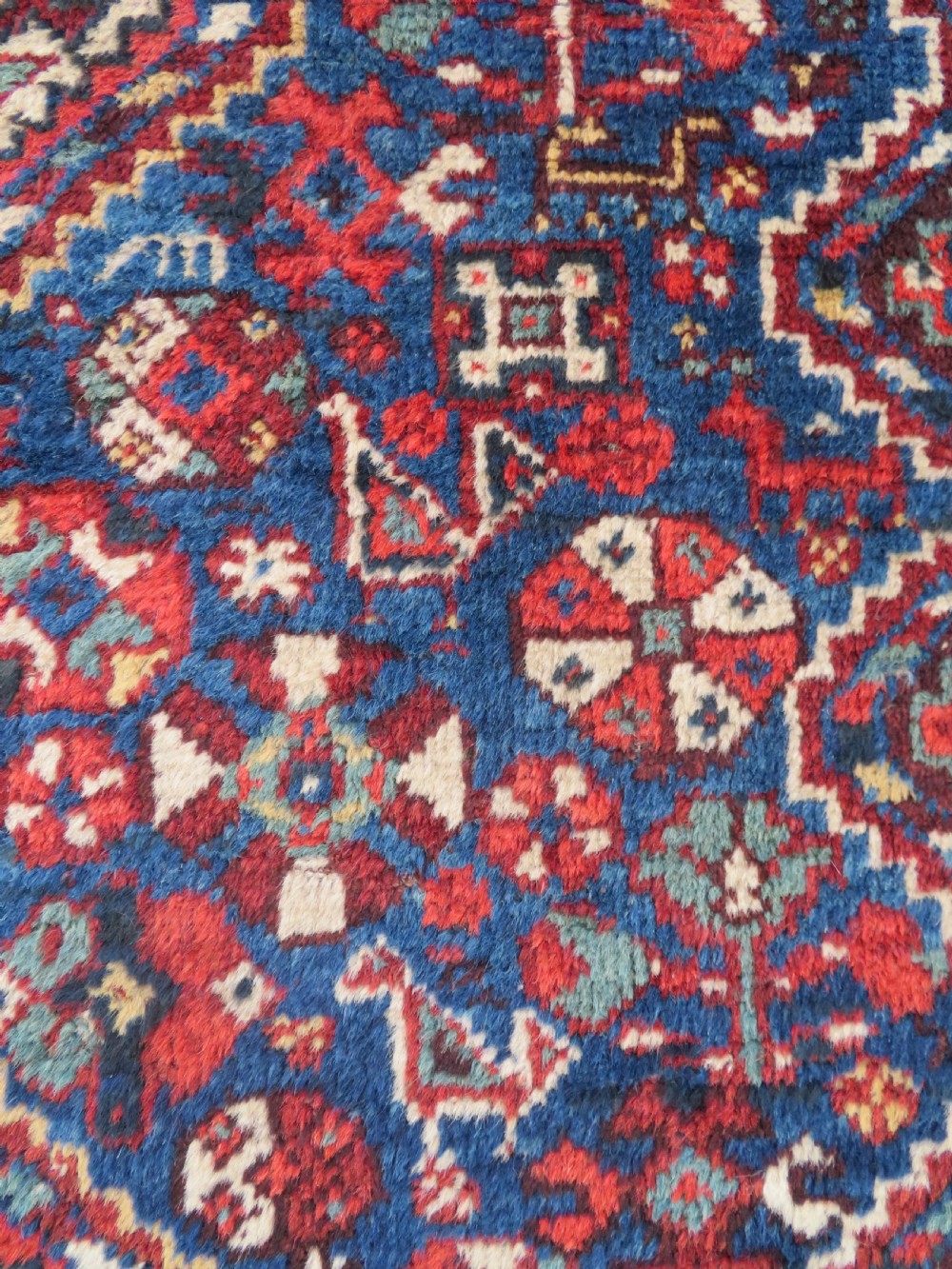 An antique South Persian Khamseh rug featuring three diamond-shaped central medallions and geometric bird motifs in shades of red, navy blue, and cream. View V