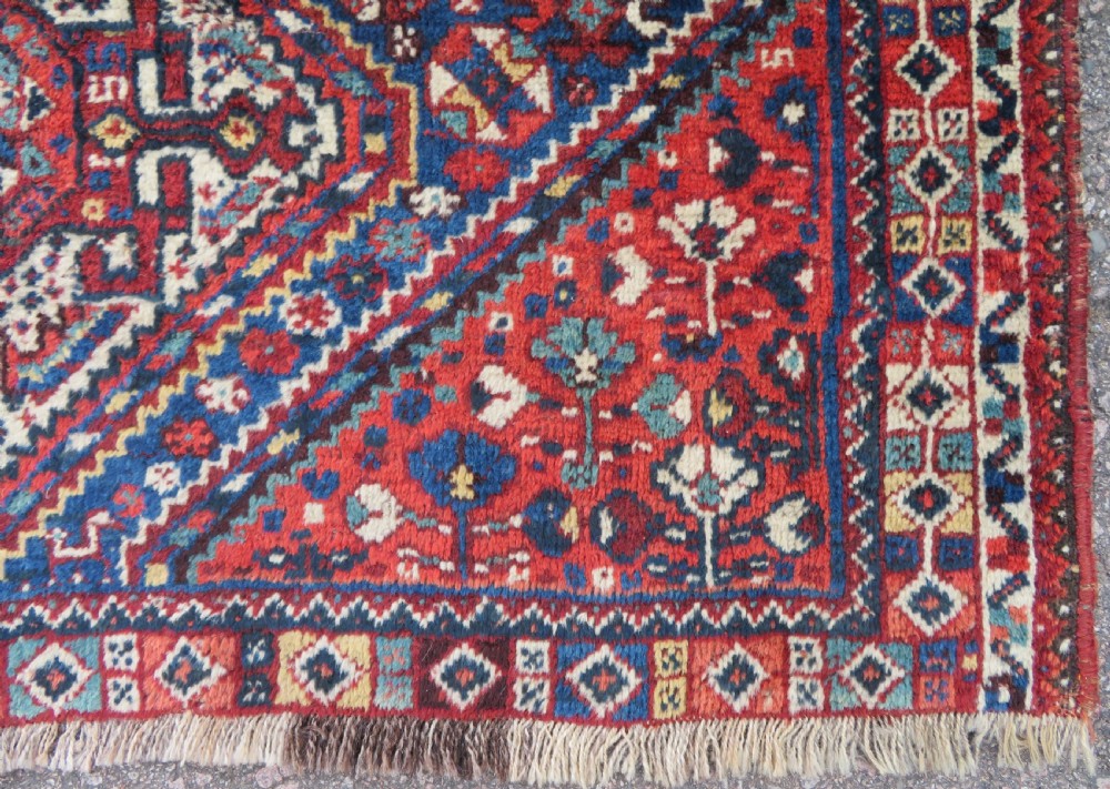 An antique South Persian Khamseh rug featuring three diamond-shaped central medallions and geometric bird motifs in shades of red, navy blue, and cream. View X