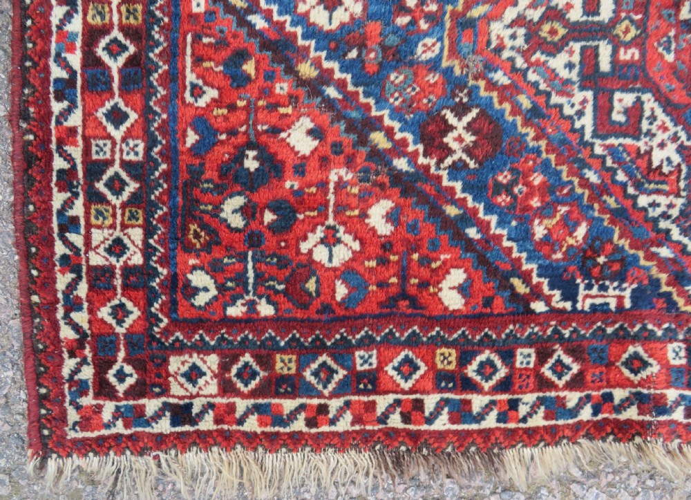 An antique South Persian Khamseh rug featuring three diamond-shaped central medallions and geometric bird motifs in shades of red, navy blue, and cream. View XII