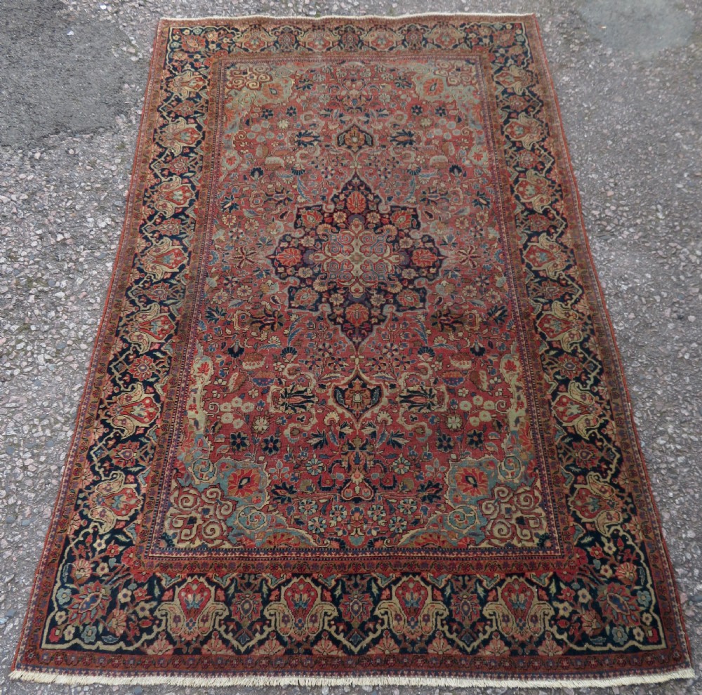 A rectangular hand-knotted wool Kashan rug featuring a central starburst medallion surrounded by dense floral patterns on a terracotta field with a navy border.