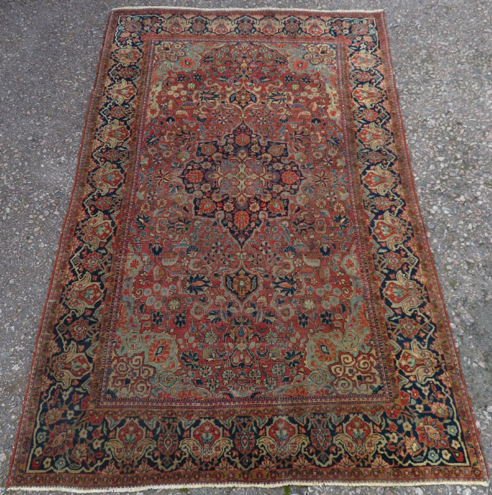 A rectangular hand-knotted wool Kashan rug featuring a central starburst medallion surrounded by dense floral patterns on a terracotta field with a navy border. View II
