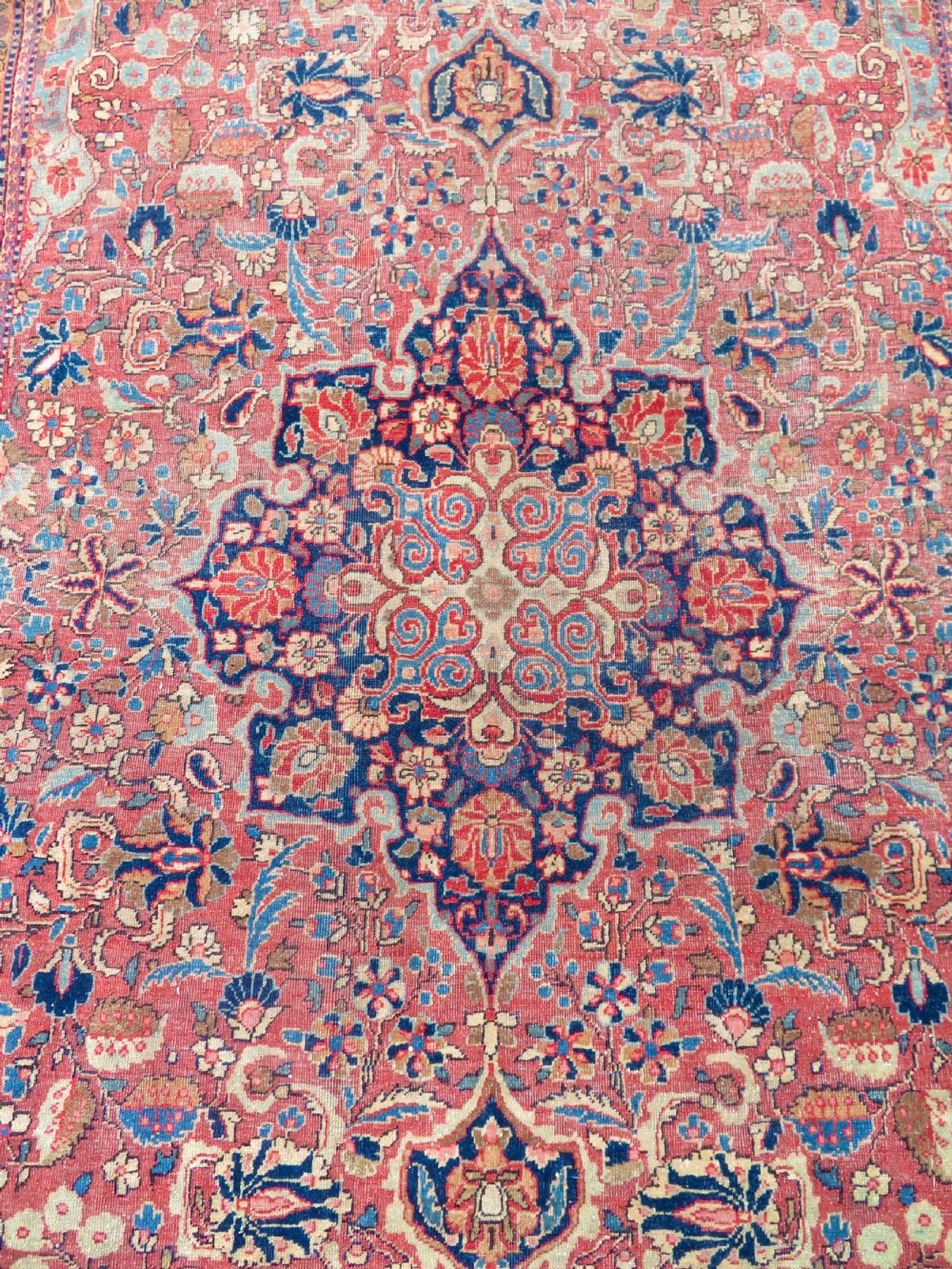 A rectangular hand-knotted wool Kashan rug featuring a central starburst medallion surrounded by dense floral patterns on a terracotta field with a navy border. View IV