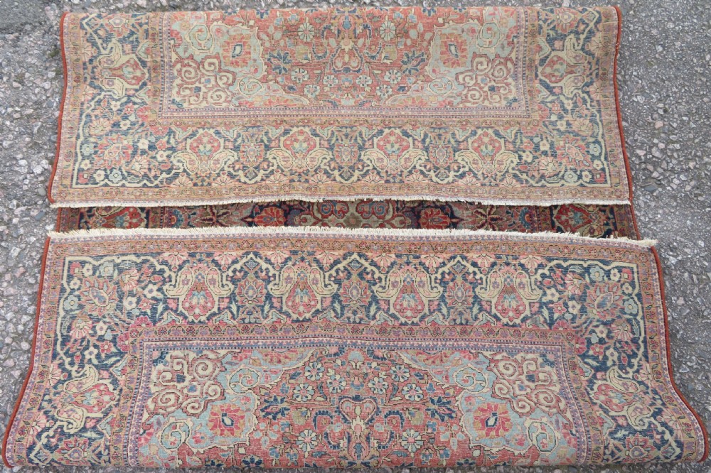 A rectangular hand-knotted wool Kashan rug featuring a central starburst medallion surrounded by dense floral patterns on a terracotta field with a navy border. View XI