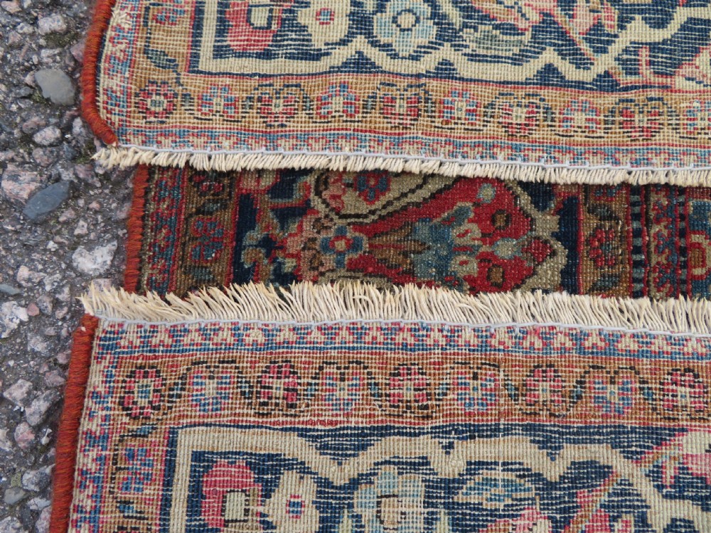 A rectangular hand-knotted wool Kashan rug featuring a central starburst medallion surrounded by dense floral patterns on a terracotta field with a navy border. View XII