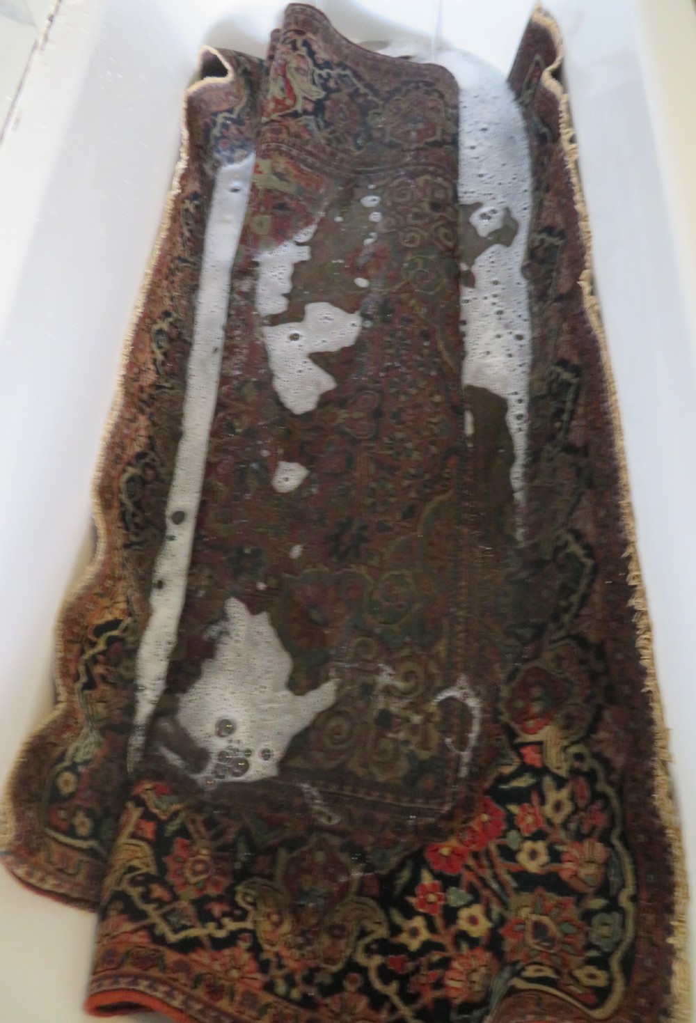 A rectangular hand-knotted wool Kashan rug featuring a central starburst medallion surrounded by dense floral patterns on a terracotta field with a navy border. View XVII