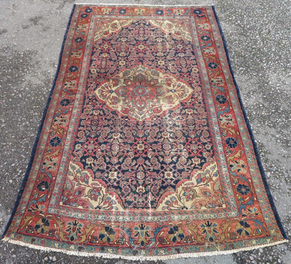 A rectangular antique Persian Malayer wool rug with a central cream and red medallion set against a dark navy field surrounded by intricate floral borders.