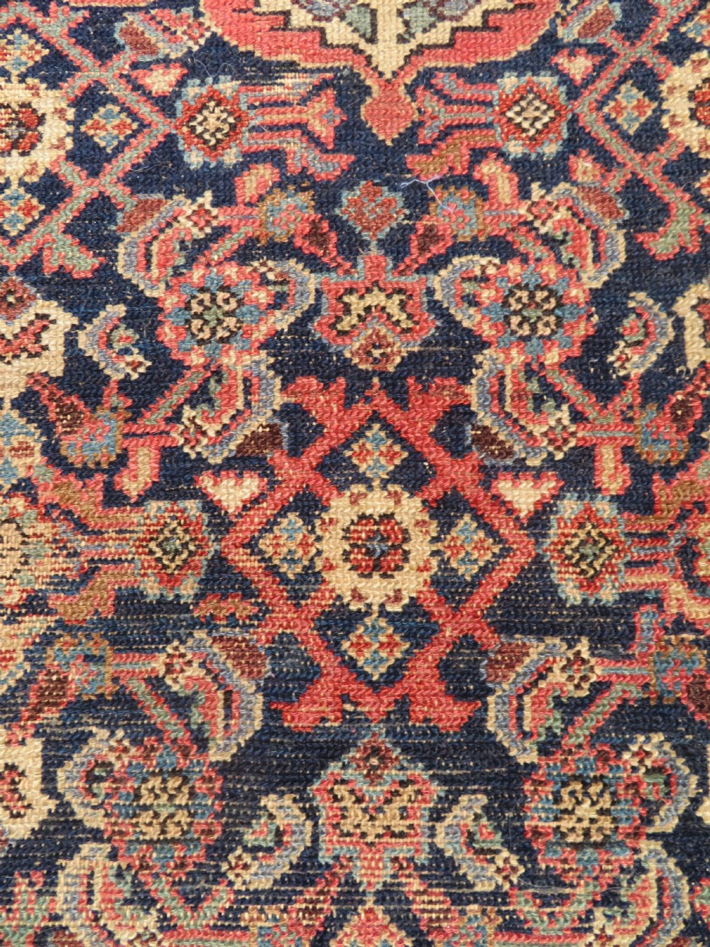 A rectangular antique Persian Malayer wool rug with a central cream and red medallion set against a dark navy field surrounded by intricate floral borders. View IV