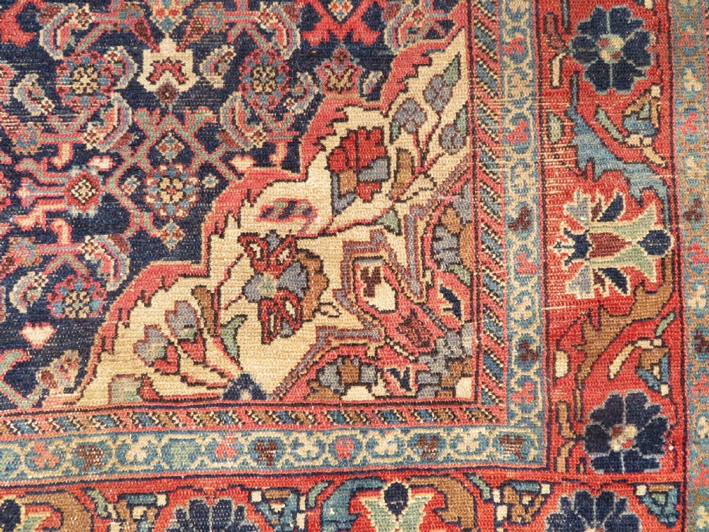 A rectangular antique Persian Malayer wool rug with a central cream and red medallion set against a dark navy field surrounded by intricate floral borders. View VI