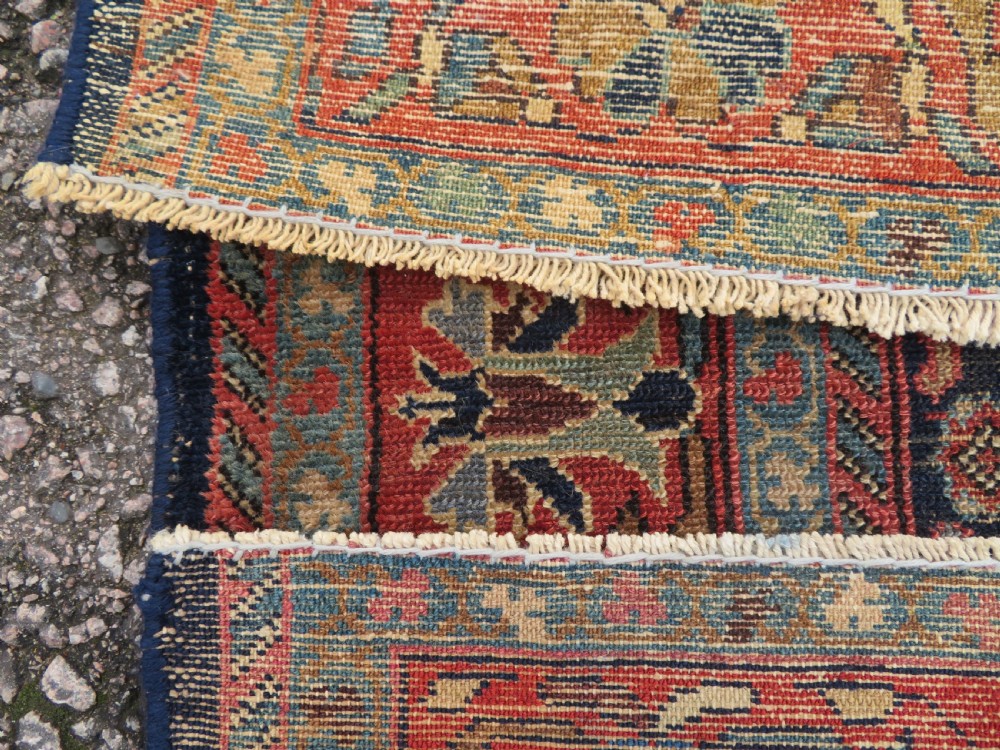 A rectangular antique Persian Malayer wool rug with a central cream and red medallion set against a dark navy field surrounded by intricate floral borders. View XIII