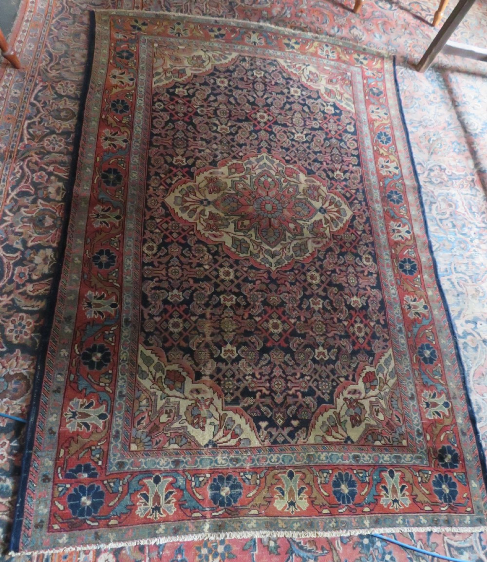 A rectangular antique Persian Malayer wool rug with a central cream and red medallion set against a dark navy field surrounded by intricate floral borders. View XV