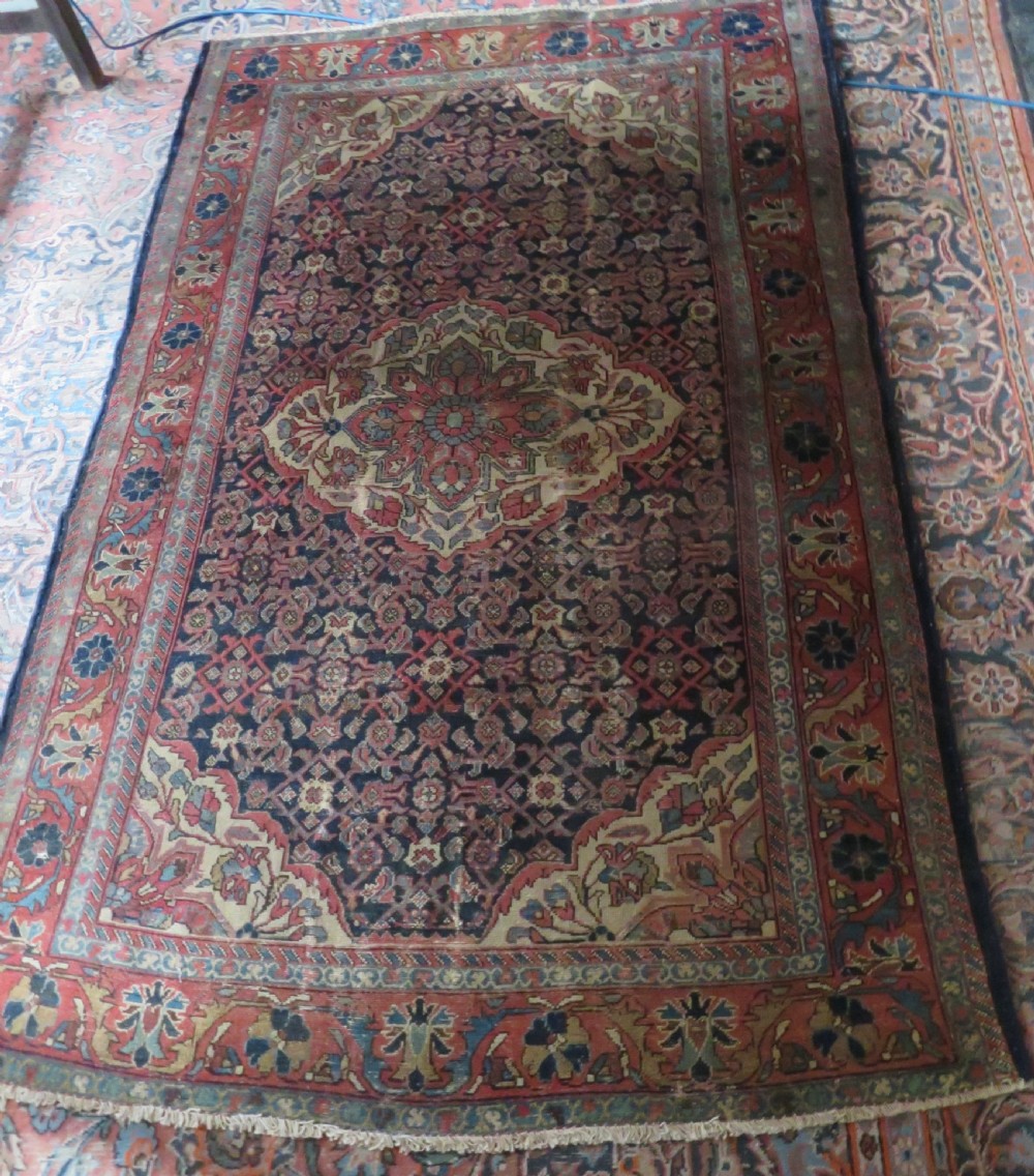 A rectangular antique Persian Malayer wool rug with a central cream and red medallion set against a dark navy field surrounded by intricate floral borders. View XVI