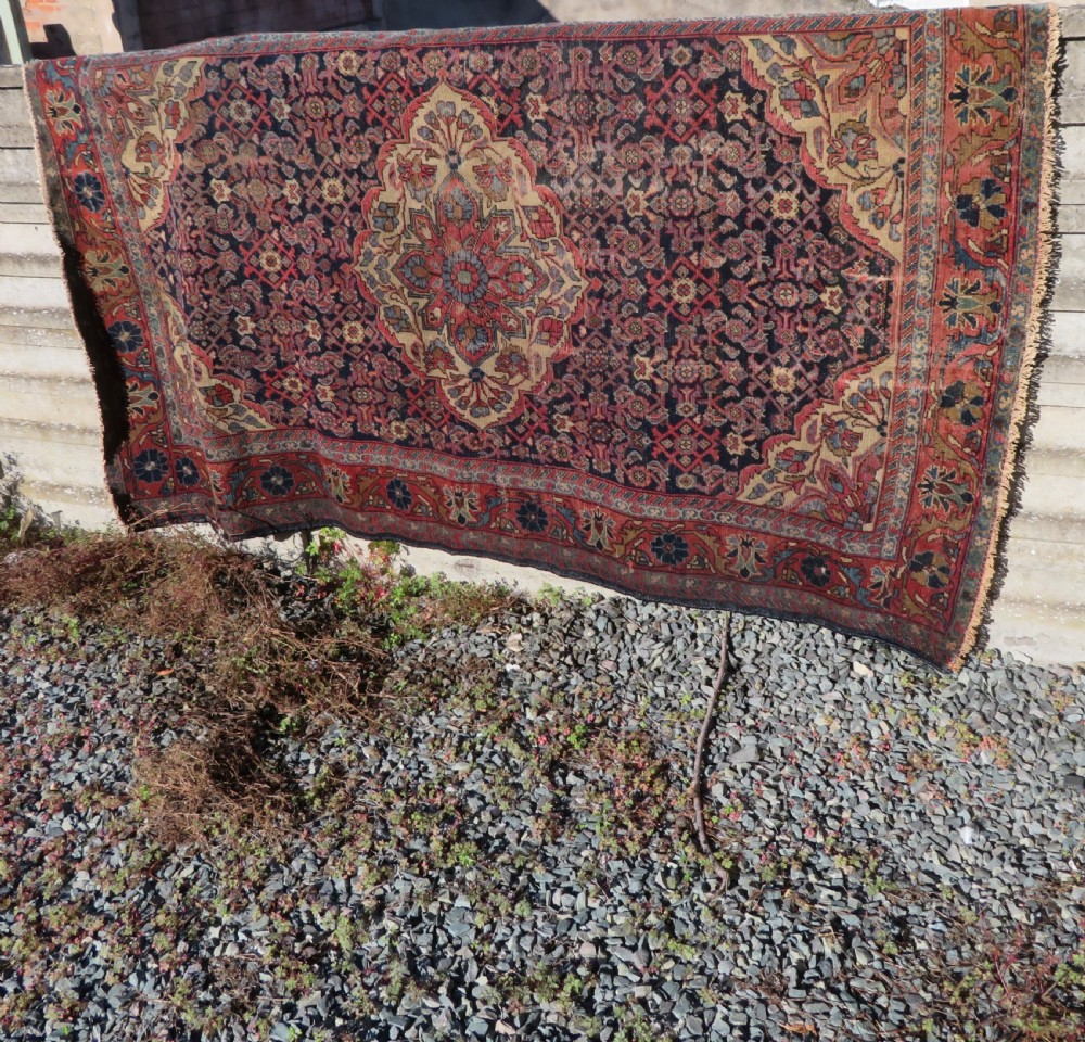 A rectangular antique Persian Malayer wool rug with a central cream and red medallion set against a dark navy field surrounded by intricate floral borders. View XVII