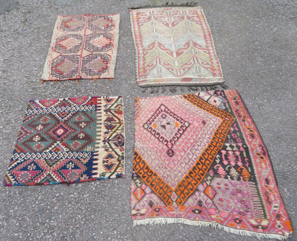 A group of four individual hand-woven Turkish kilim mats featuring vibrant geometric patterns, diamond medallions, and zig-zag borders.