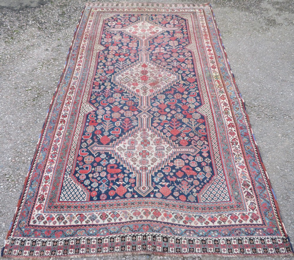 An antique hand-knotted Khamseh tribal wool rug featuring three geometric pole medallions in navy blue, terracotta red, and cream with detailed borders.