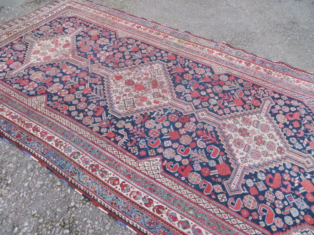An antique hand-knotted Khamseh tribal wool rug featuring three geometric pole medallions in navy blue, terracotta red, and cream with detailed borders. View IV