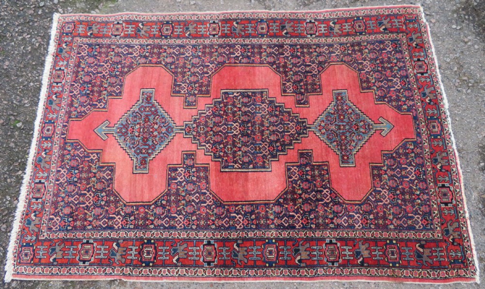 An antique West Persian Senneh wool rug featuring a navy blue stepped diamond medallion centered on a terracotta red field with intricate geometric borders. View II