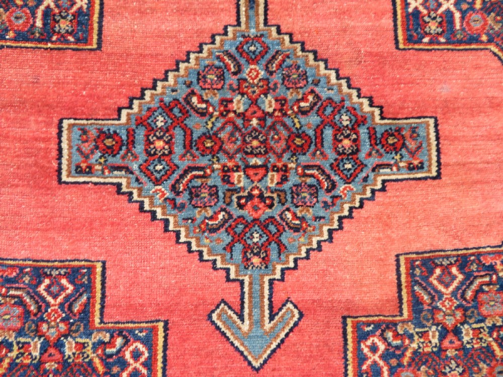 An antique West Persian Senneh wool rug featuring a navy blue stepped diamond medallion centered on a terracotta red field with intricate geometric borders. View IV