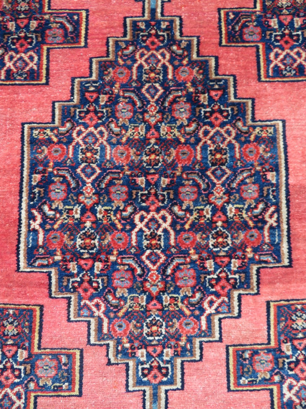 An antique West Persian Senneh wool rug featuring a navy blue stepped diamond medallion centered on a terracotta red field with intricate geometric borders. View V