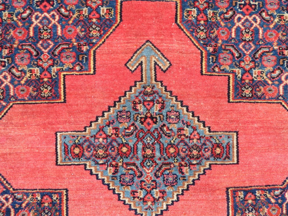 An antique West Persian Senneh wool rug featuring a navy blue stepped diamond medallion centered on a terracotta red field with intricate geometric borders. View VI
