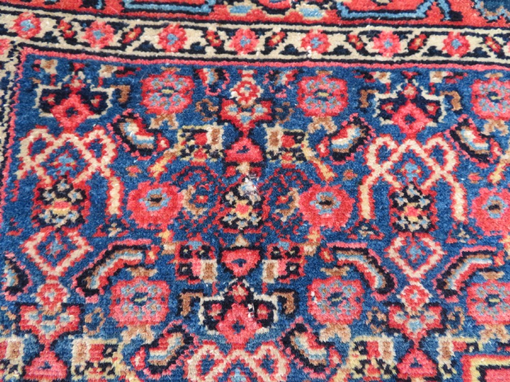 An antique West Persian Senneh wool rug featuring a navy blue stepped diamond medallion centered on a terracotta red field with intricate geometric borders. View VII