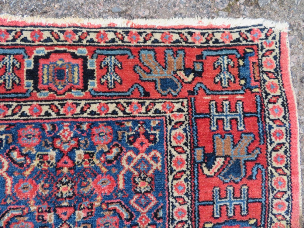 An antique West Persian Senneh wool rug featuring a navy blue stepped diamond medallion centered on a terracotta red field with intricate geometric borders. View IX