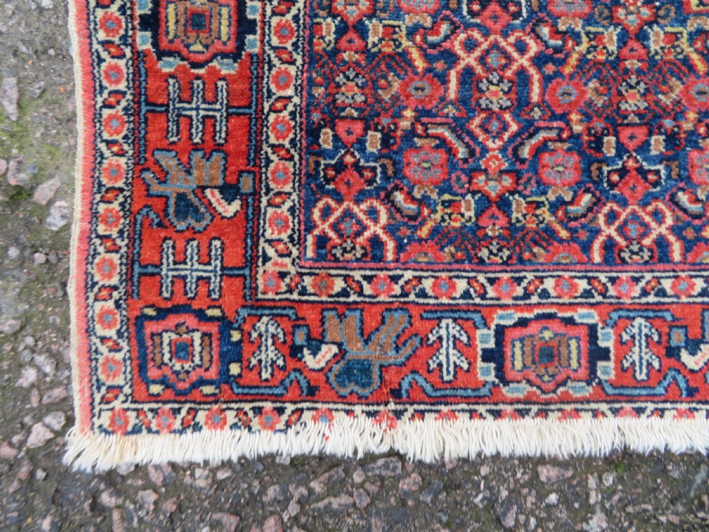 An antique West Persian Senneh wool rug featuring a navy blue stepped diamond medallion centered on a terracotta red field with intricate geometric borders. View X
