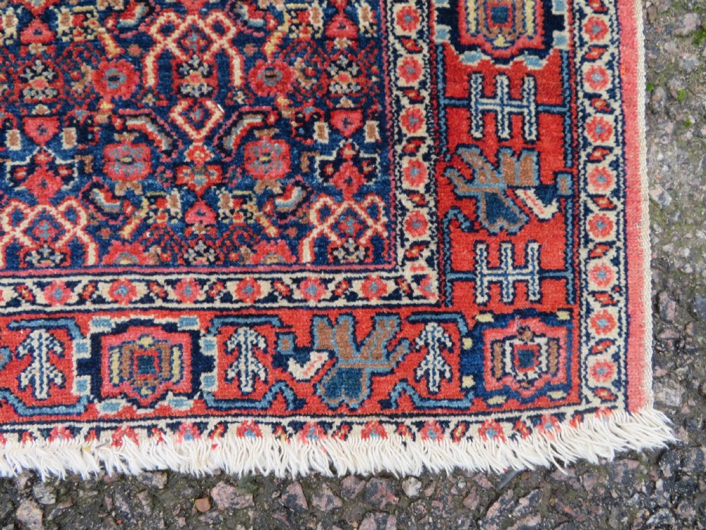 An antique West Persian Senneh wool rug featuring a navy blue stepped diamond medallion centered on a terracotta red field with intricate geometric borders. View XI