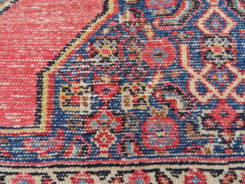 An antique West Persian Senneh wool rug featuring a navy blue stepped diamond medallion centered on a terracotta red field with intricate geometric borders. View XVI