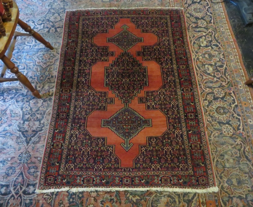 An antique West Persian Senneh wool rug featuring a navy blue stepped diamond medallion centered on a terracotta red field with intricate geometric borders. View XVII