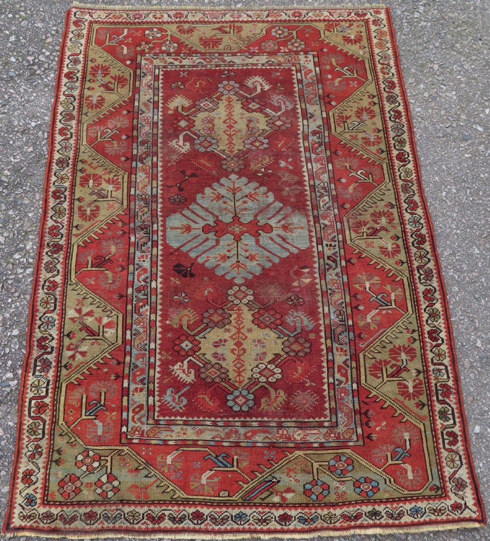 An antique handwoven Anatolian Ada Melas wool rug featuring central geometric medallions in grey, red, and ochre framed by detailed botanical borders.
