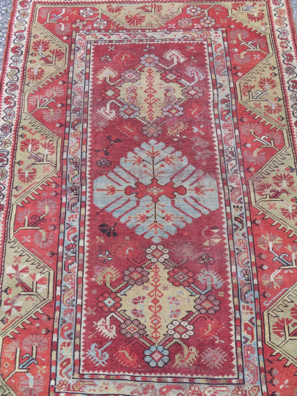 An antique handwoven Anatolian Ada Melas wool rug featuring central geometric medallions in grey, red, and ochre framed by detailed botanical borders. View II