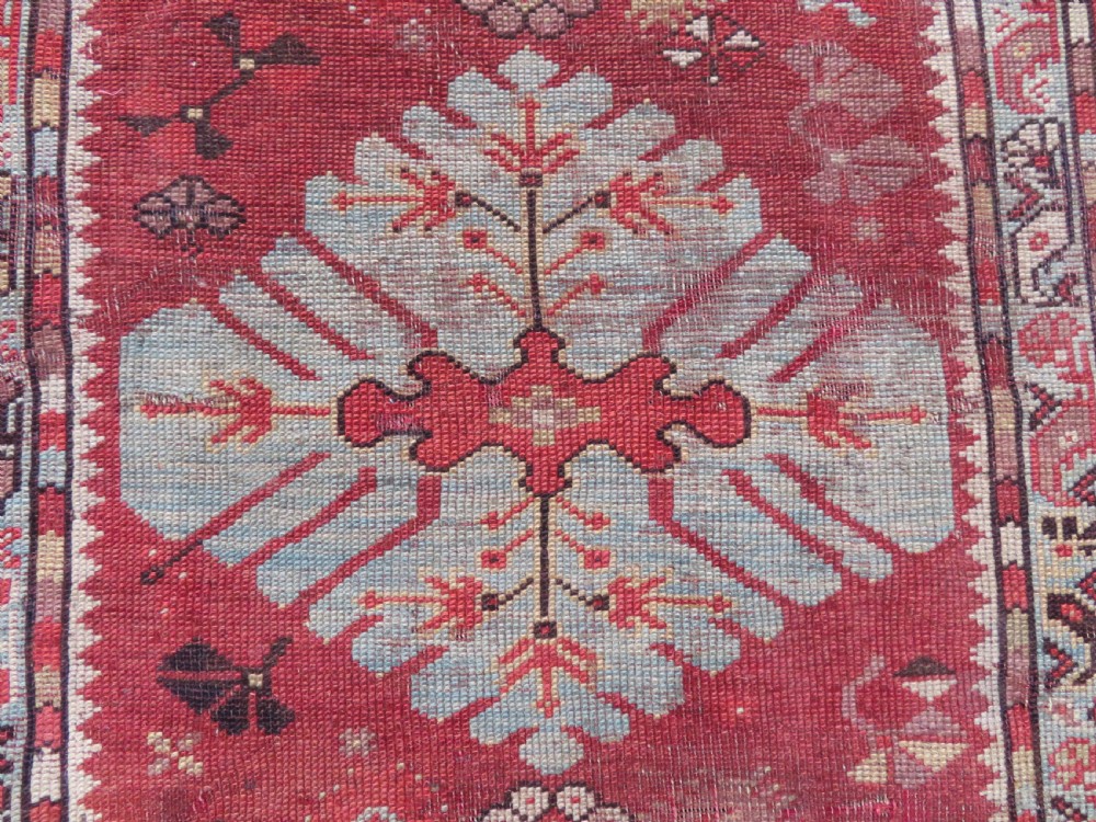 An antique handwoven Anatolian Ada Melas wool rug featuring central geometric medallions in grey, red, and ochre framed by detailed botanical borders. View III