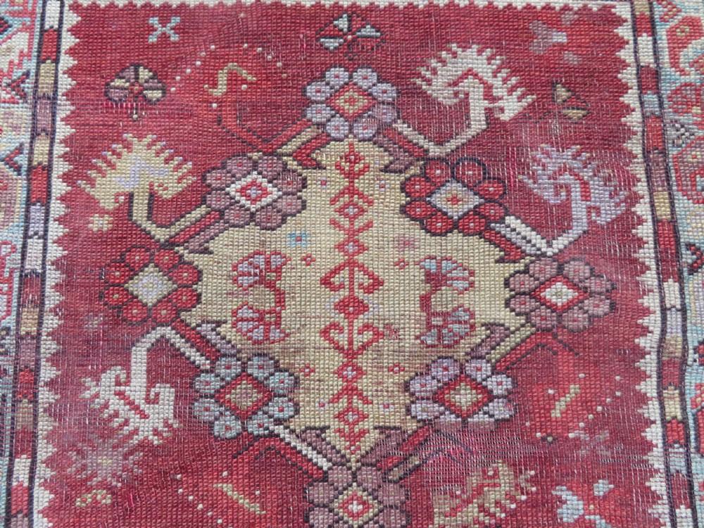 An antique handwoven Anatolian Ada Melas wool rug featuring central geometric medallions in grey, red, and ochre framed by detailed botanical borders. View IV