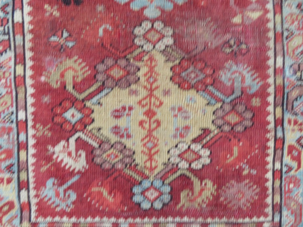 An antique handwoven Anatolian Ada Melas wool rug featuring central geometric medallions in grey, red, and ochre framed by detailed botanical borders. View V