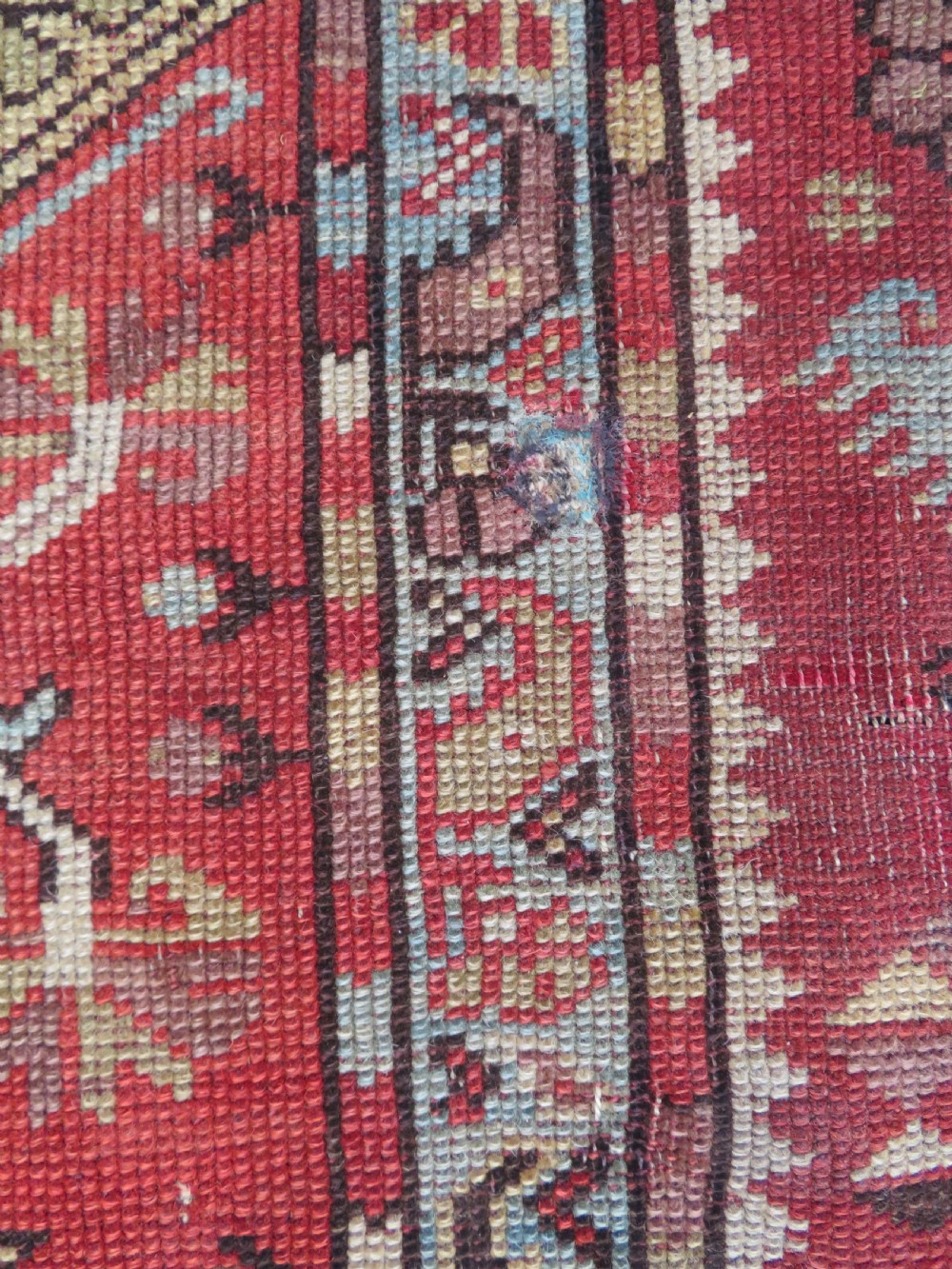 An antique handwoven Anatolian Ada Melas wool rug featuring central geometric medallions in grey, red, and ochre framed by detailed botanical borders. View VII