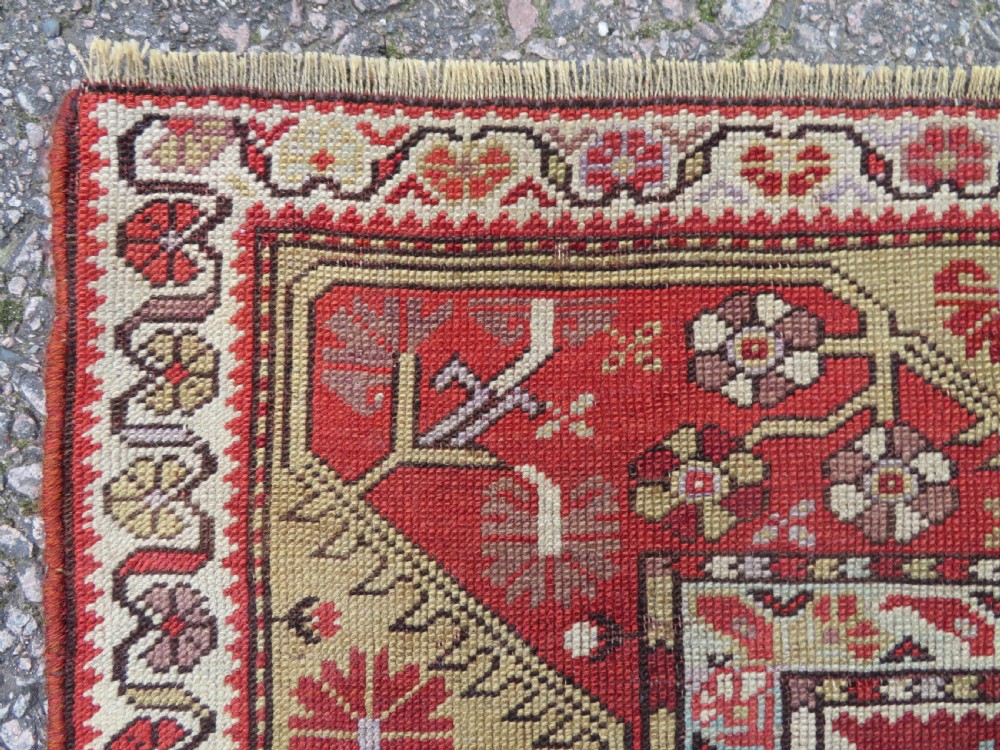 An antique handwoven Anatolian Ada Melas wool rug featuring central geometric medallions in grey, red, and ochre framed by detailed botanical borders. View IX