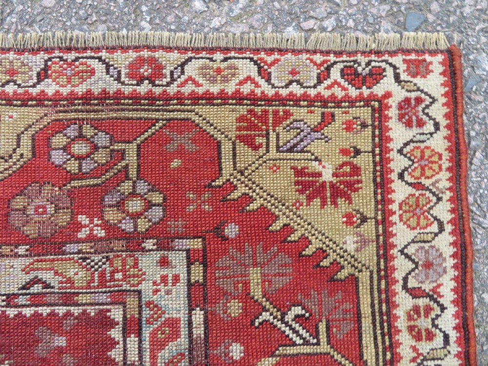 An antique handwoven Anatolian Ada Melas wool rug featuring central geometric medallions in grey, red, and ochre framed by detailed botanical borders. View X