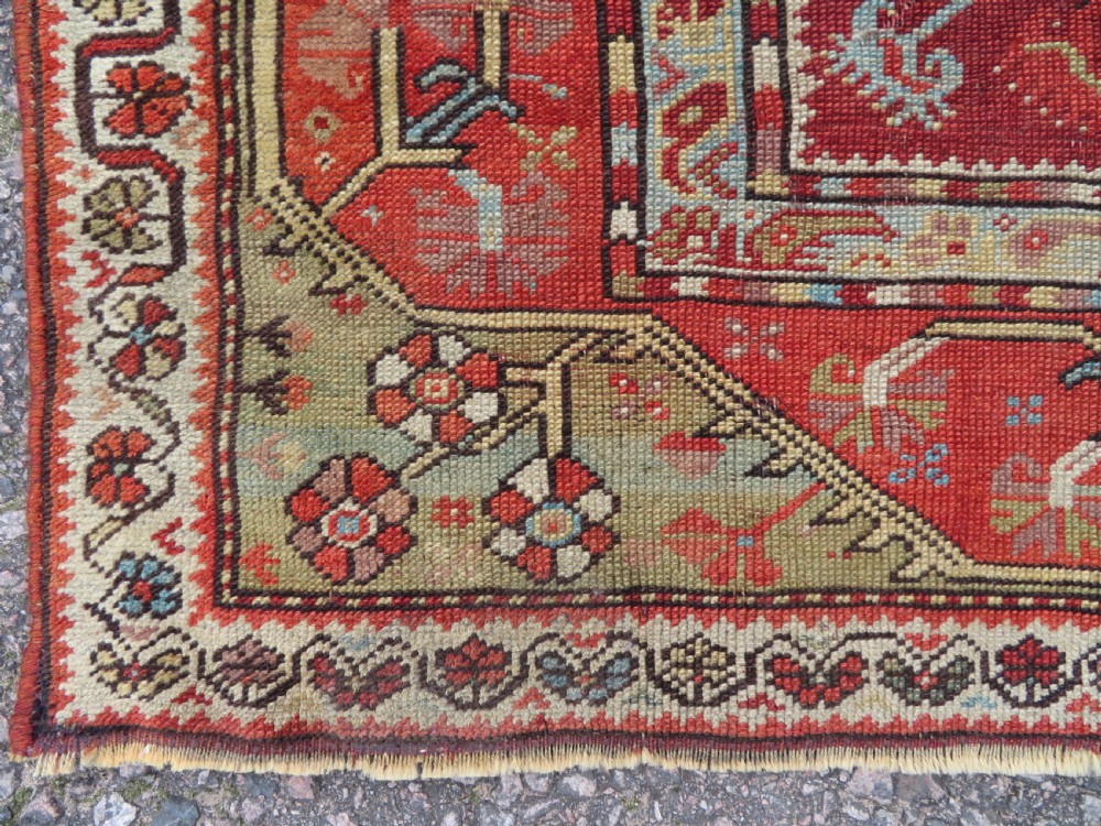An antique handwoven Anatolian Ada Melas wool rug featuring central geometric medallions in grey, red, and ochre framed by detailed botanical borders. View XI