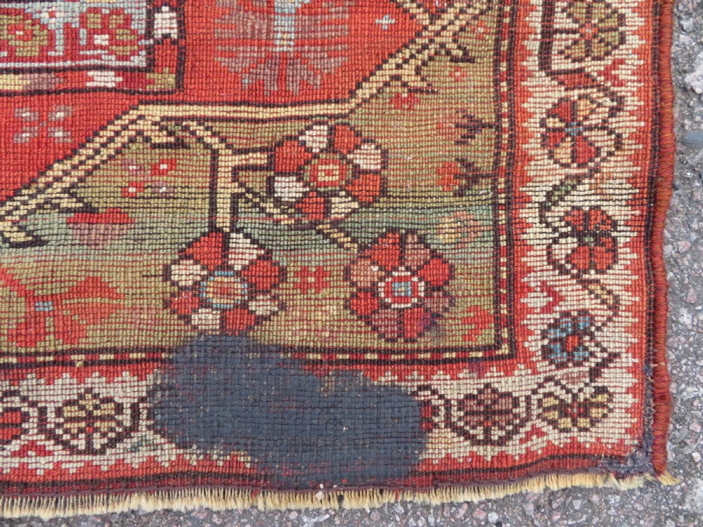 An antique handwoven Anatolian Ada Melas wool rug featuring central geometric medallions in grey, red, and ochre framed by detailed botanical borders. View XVI