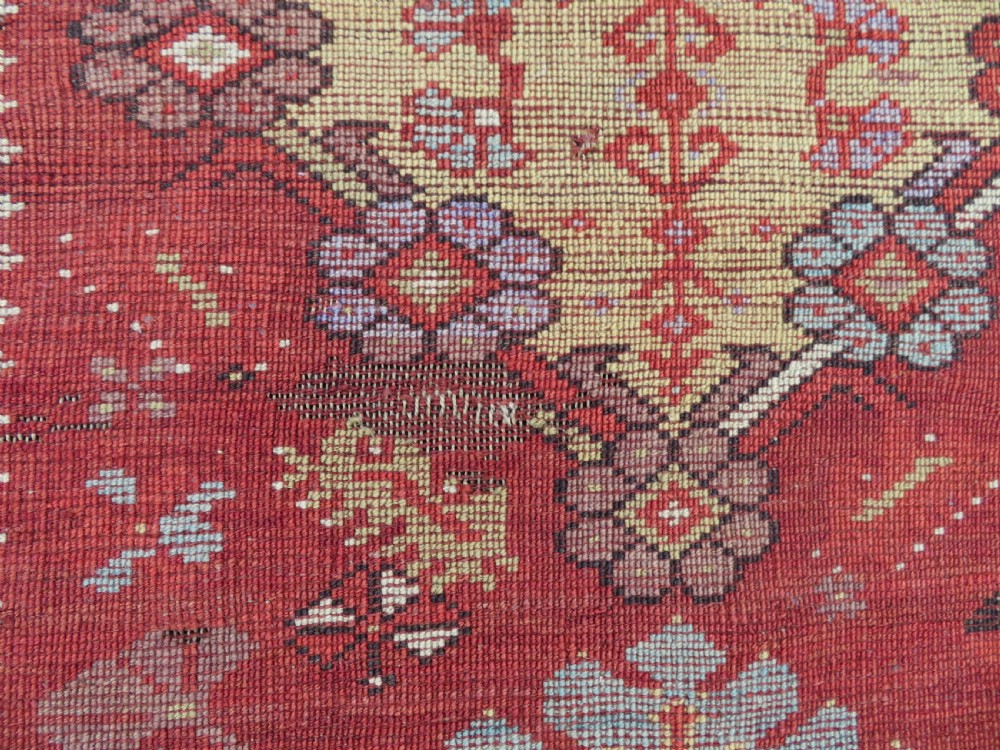 An antique handwoven Anatolian Ada Melas wool rug featuring central geometric medallions in grey, red, and ochre framed by detailed botanical borders. View XVII