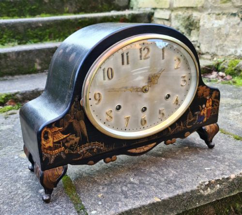 fig 1. An antique black lacquered mantel clock decorated with gold chinoiserie scenes and an oval brass-rimmed clock face.