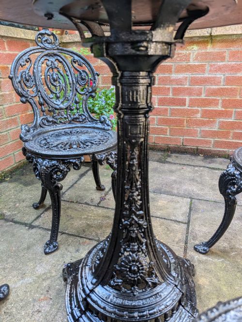 fig 4. A Victorian cast-iron garden set featuring a circular copper-topped pedestal table surrounded by four ornate black cast-iron chairs with foliage-patterned backrests.