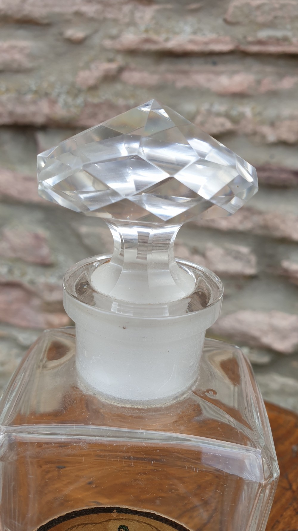 A clear glass rectangular perfume bottle with a faceted geometric stopper and an original circular paper label reading Potter and Moores Mitcham Lavender. View III